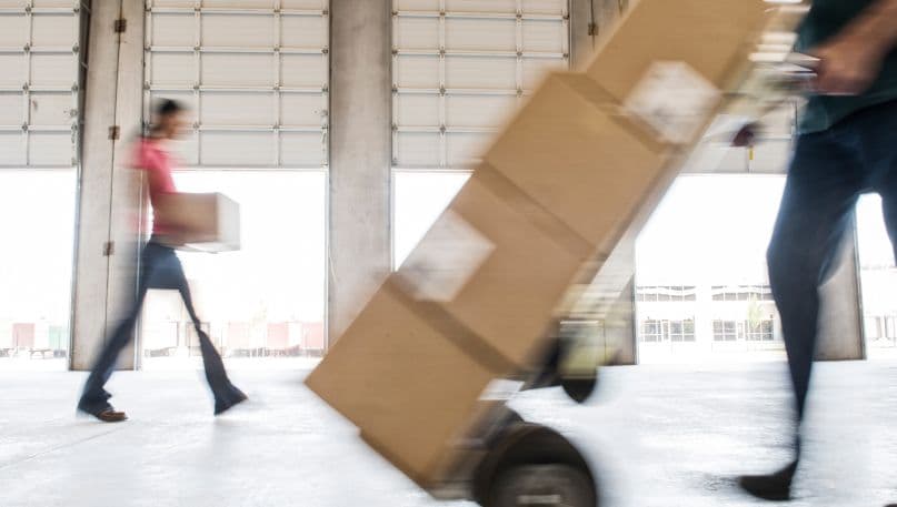 People walking through a warehouse holding boxes. 