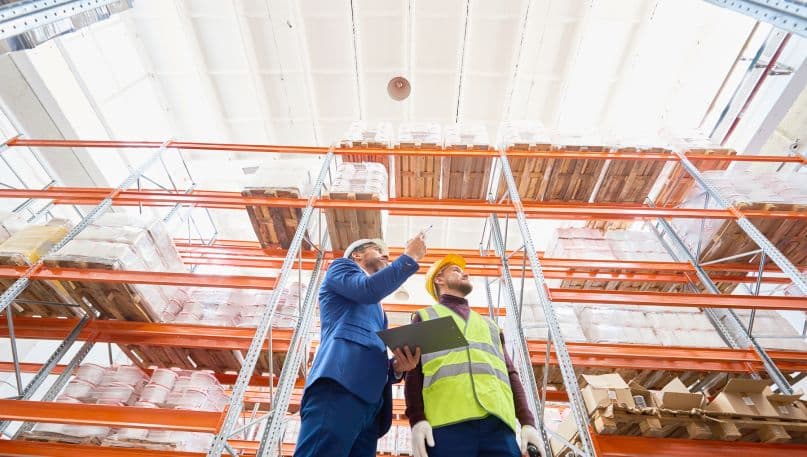 Two men taking inventory of items on shelves inside of a warehouse